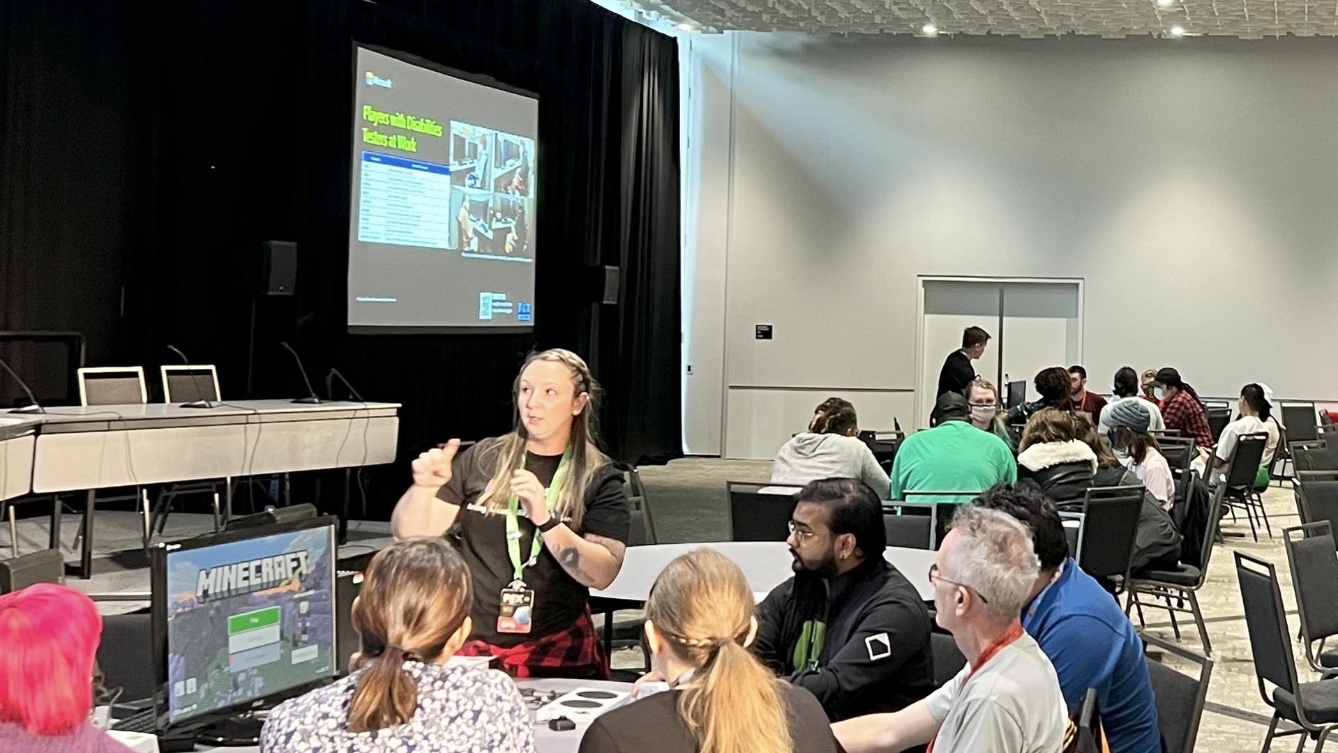 A member of Xbox’s Accessibility Team presents to a group of people gathered around a table, informing them about The Microsoft Gaming Accessibility Testing Service.