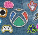 The Xbox logo as a patch sewn onto a denim jacket. The Xbox logo is surrounded by other patch versions of accessibility logos including the Xbox Adaptive Controller, the Game Accessibility Joyrider, the disability pride logo, and more.