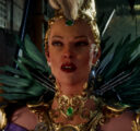 Lady Ironwood, adorned with ornate gold jewelry and green feathers, stands half-lit in shadow, staring menacingly as she speaks.