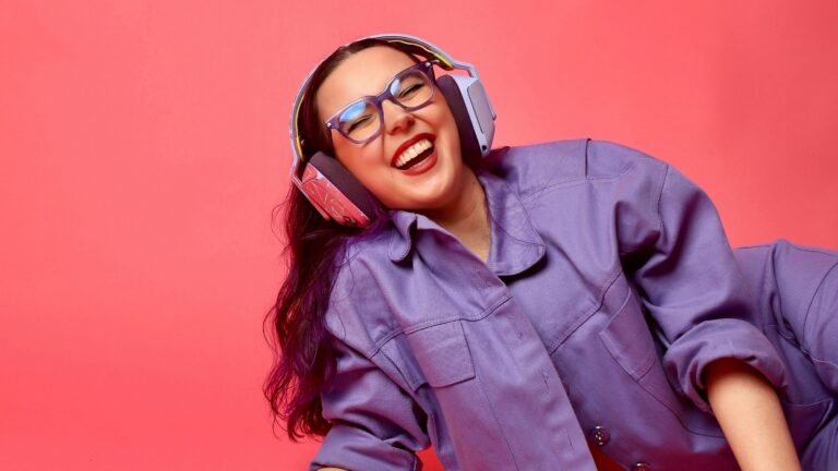 Imagem da criadora de conteúdo Ana Xisdê - ela sorri enquanto escuta algo no fone de ouvido